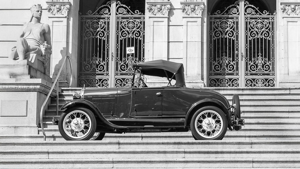 stari automobil model T ispred zgrade sa stepenicama i skulpturom u crno-beloj fotografiji