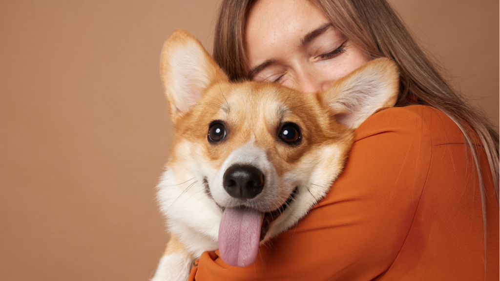Mlada žena grli psa, pas sa isplaženim jezikom gleda u kameru
